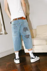 Bermuda de jean de corte baggy, lavado celeste con efecto desgastado. Presenta bordados grandes en los bolsillos traseros con caracteres chinos en negro y blanco. Tiene un parche de cuero marrón en la cintura trasera.