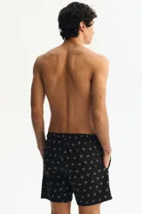 Short de baño negro de sirsaca con estampado de palmeras blancas, cintura elástica con cordón de ajuste blanco y bolsillos laterales.