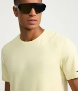 Remera deportiva de hombre con tecnología dry fit, cuello redondo y manga corta. Presenta un diseño liso en color beige con una pequeña etiqueta decorativa en el dobladillo.