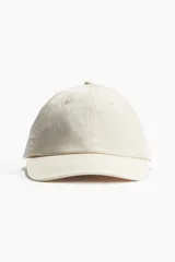 Gorra color crema de sarga de algodón con ojales bordados y correa ajustable con hebilla metálica en la parte posterior.