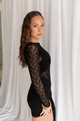 Vestido corto negro de encaje transparente, con mangas largas y falda ajustada con detalle lateral asimétrico tipo pareo.