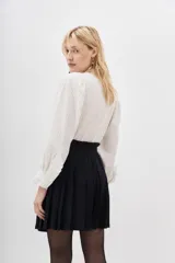 Falda corta negra plisada, de tiro alto con pretina ancha.
