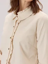 Camisa de algodón con cuello clásico y detalle de volados en la cartera delantera. Presenta mangas largas con puños abotonados y un diseño de corte recto.