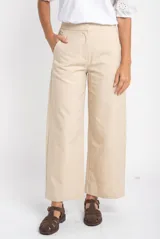 Pantalón de corte baggy y tiro medio, confeccionado en algodón peinado de color arena. Presenta diseño de pierna ancha, cierre frontal con botón y bolsillos laterales.