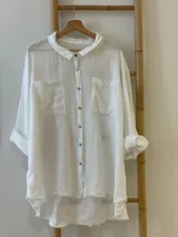 Camisa blanca de lino con terminaciones desflecadas, cuello clásico, cierre frontal con botones, dos bolsillos de parche en el pecho y mangas largas con puños abotonados.