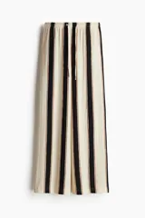 Pantalón de punto de corte holgado con piernas amplias y tiro alto, cintura elástica con cordón de ajuste y diseño a rayas verticales en tonos blanco, negro y marrón.