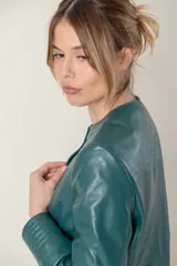 Campera de cuero ovino italiano color verde azulado, con cuello mao, cierre frontal con broches ocultos, bolsillos laterales y detalle de capitoneado en puños y bolsillos.