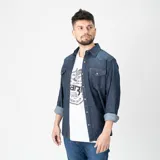 Camisa de denim azul con cuello clásico, cierre con botones a presión, mangas largas con puños abotonados y dos bolsillos con solapa abotonada en el pecho. Corte regular.