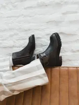 Bota corta de cuero color gris y beige, con detalle de correa marrón con hebilla y tachas plateadas. Tiene suela de goma negra y taco de madera.