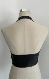 Top negro tipo chaleco de cuero sintético, con escote halter y cierre frontal con hebilla.