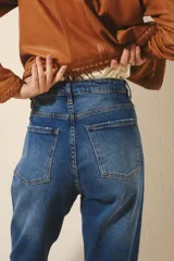 Jean de tiro alto en denim azul con lavado localizado y efecto de bigotes. Presenta un corte de pierna recta y cierre frontal con botón y cremallera.