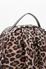Mochila de diseño urbano con estampado animal print de leopardo, confeccionada en material resistente y liviano. Presenta compartimento principal con cierre, bolsillo frontal amplio con detalle de cuero sintético negro y bolsillos laterales. Incluye manija superior y tiras regulables.