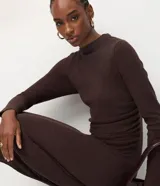 Vestido midi de punto color marrón chocolate, con manga larga, cuello alto sutil y detalle de fruncido lateral que ajusta la silueta. Diseño minimalista de corte recto.