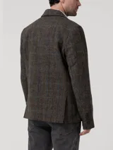 Blazer de lana Harris Tweed con patrón de espiga y cuadros sutiles en tonos tierra, azul y naranja. Presenta cierre frontal de dos botones, solapas clásicas y bolsillos con solapa. Incluye forro interior satinado.