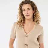 Sweater de punto en color beige, de manga corta y corte ajustado. Presenta un escote en V y cierre frontal con botones decorativos dorados en forma de concha.