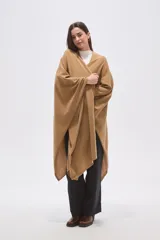 Poncho abierto de corte asimétrico y holgado, confeccionado en tejido de punto suave color beige, con mangas amplias y caída fluida.