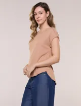 Remera blanca de punto acanalado con escote redondo adornado con tachas metálicas en el cuello y hombros, mangas cortas japonesas y ruedo curvo.