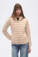 Campera acolchada tipo puffer, color beige claro, con capucha y cierre frontal. Presenta costuras horizontales y un calce entallado.