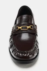 Mocasín plano de mujer con acabado acharolado color bordó. Presenta un diseño con fruncidos en el empeine y una hebilla metálica dorada decorativa. Cuenta con punta redonda y suela plana de 2,5 cm.