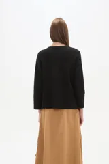 Sweater negro liso, holgado, con cuello a la base y broches decorativos en el lateral.