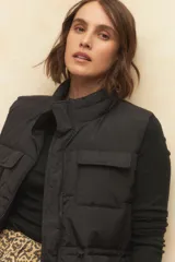 Chaleco puffer negro de cuello alto, con cierre frontal y cuatro bolsillos con solapa. Cuenta con cintura ajustable con cordón.