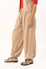 Pantalon tipo babucha de color beige, con silueta relajada y acabado suave tipo piel de durazno. Presenta cintura regulable con cordón y elástico en los tobillos que genera una forma abuchonada.