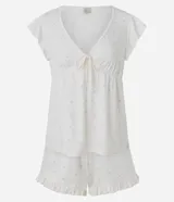 Pijama corto de dos piezas en color blanco con estampado continuo de pequeños corazones rosados. Incluye una blusa con escote en V, mangas cortas con volados, lazo frontal bajo el busto y un short con cintura elastizada y volados en los bajos.