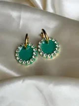 Aros colgantes dorados con dije circular de resina color turquesa, bordeado con strass. El arito es de acero quirúrgico.