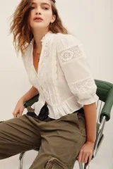 Camisa blanca de algodón con detalles de encaje broderie y transparencias, escote en V con cuello alto con volados, y mangas cortas abullonadas.