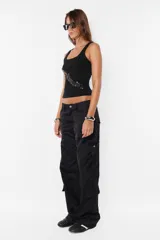 Pantalón cargo negro de corte recto y tiro bajo, con recortes y múltiples bolsillos laterales y traseros con tapa y botón a presión. Cierre frontal con cremallera de nylon y botón personalizado.
