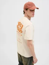 Camiseta color crema de algodón con cuello redondo y estampado en el frente y la espalda con la leyenda "Originals Urban Aesthetics Certified Daily Basic Garments Designed in the Holmen District by Team Originals Est. Copenhagen 1990 Creative Community".