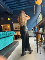 Pollera midi negra de cuero sintético con abertura frontal y flecos largos en el ruedo. Se combina con un crop top haciendo juego y botas de caña baja.