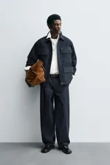 Pantalón de corte barrel fit confeccionado en denim de algodón rígido color azul oscuro. Presenta cintura con pliegues frontales, bolsillos laterales y bolsillos traseros de vivo. Cierre frontal con cremallera y gancho metálico oculto.
