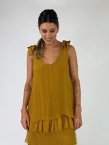 Top de viscosa color mostaza, sin mangas, con escote redondo y detalle de moños para atar en los breteles. Presenta un diseño holgado con doble capa y volados en el borde inferior.