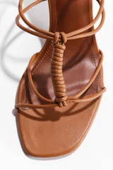 Sandalias de taco alto con tiras finas, color suela, punta cuadrada y diseño con nudo decorativo delantero. Tienen pulsera ajustable con hebilla en el tobillo y taco cuadrado.