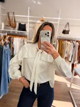 Camisa de color rojo intenso con volados en los hombros y lazo ajustable en el cuello. Presenta un cierre frontal con botones y un diseño de calce amplio.
