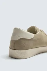 Zapatilla de cordones para hombre, fabricada en piel con acabado serraje (gamuza) color beige claro. Presenta detalles de pespuntes y una suela gruesa de goma a contraste en color crema.