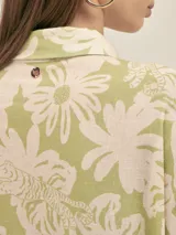 Vestido camisero de corte oversize, con cuello clásico, cierre frontal de botones y mangas cortas. Presenta un estampado floral en tonos verde y beige, bolsillos laterales y un diseño holgado.