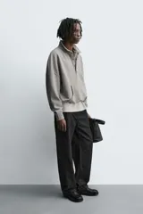 Sudadera de corte boxy fit en color gris, confeccionada en tejido de algodón con interior afelpado. Presenta cuello solapa, cierre frontal con botones a presión, manga larga con puños acanalados y bolsillo frontal tipo canguro. El bajo cuenta con un acabado elástico.