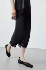 Falda midi de tiro alto confeccionada en tejido efecto piel color negro. Presenta un diseño de corte recto con bajo acabado en aplicación de encaje a tono y abertura en la espalda. Cierre mediante cremallera oculta en la costura posterior.