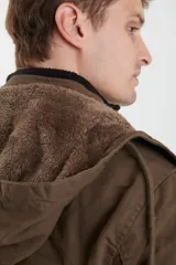 Campera de abrigo estilo parka, color verde militar, con capucha desmontable, cierre frontal con botones y múltiples bolsillos funcionales en pecho, cintura y manga.