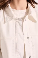 Sobrecamisa color blanco hueso de algodón, con cuello camisero, cierre frontal con botones a presión metálicos, bolsillos de parche en el pecho y bordados florales en los hombros. Corte holgado.