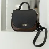 Cartera de cuero negra y marrón con correa larga ajustable y cierre metálico plateado.