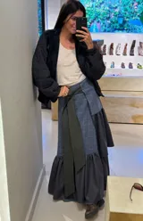 Falda larga tipo patchwork confeccionada en diferentes texturas de tweed a cuadros. Presenta un diseño envolvente con un lazo frontal en color verde oscuro y un ruedo con volados amplios en tela de cuadros más pequeños.