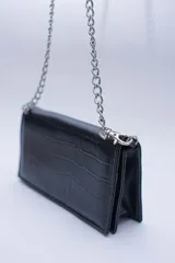 Cartera negra con textura símil cocodrilo y cadena metálica plateada.