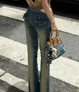 Jean de tiro bajo con efecto desgastado y costuras decorativas que realzan la silueta. Presenta un corte ajustado en la cadera y muslos con una leve apertura acampanada en la botamanga, incorporando un cierre frontal visible.