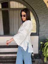 Blusa blanca de broderie con cuello mao y escote en V, mangas largas acampanadas y bordados calados.