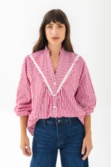 Camisa blanca de corte holgado con cuello mao y volados decorativos en el frente. Presenta cierre frontal con botones, mangas largas con puños elásticos y detalles de costuras caladas.