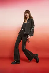 Campera de jean con lavado oscuro rojizo/marrón, estilo trucker. Presenta tachas doradas a lo largo de los bordes de los bolsillos, el canesú y los puños. Posee un bordado en relieve de diseño floral en la manga.