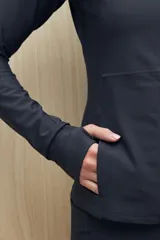 Campera deportiva negra de calce entallado, con cierre frontal completo, capucha integrada y mangas largas con puños envolventes. Presenta costuras estratégicas que estilizan la silueta y bolsillos laterales funcionales.